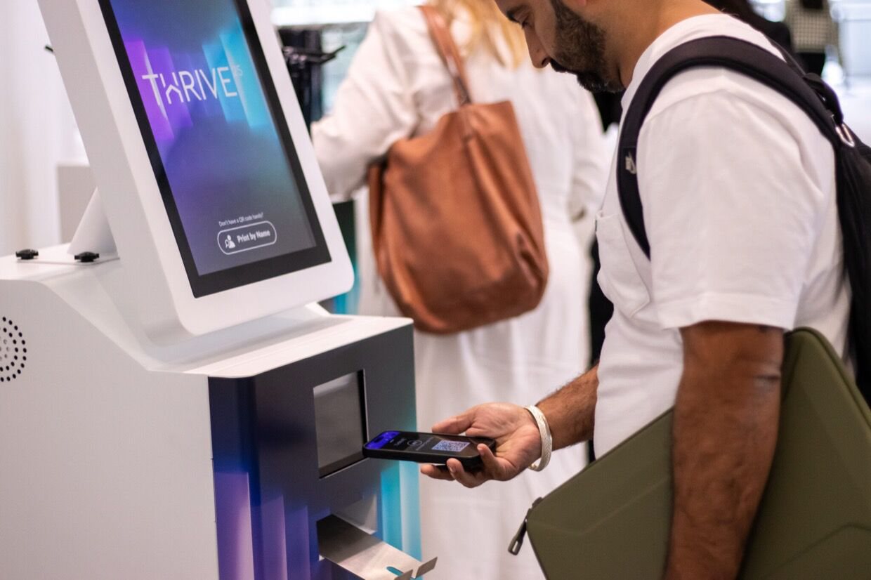 A delegate scanning a QR code at a Thrive-branded Max kiosk