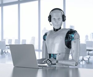 White humanoid robot wearing a headset, seated at an office desk typing on a laptop