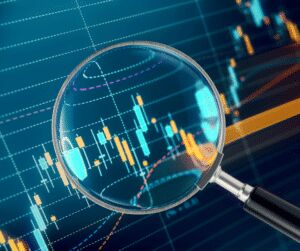 Magnifying glass held over a dark screen of candlestick and line charts in blue and orange