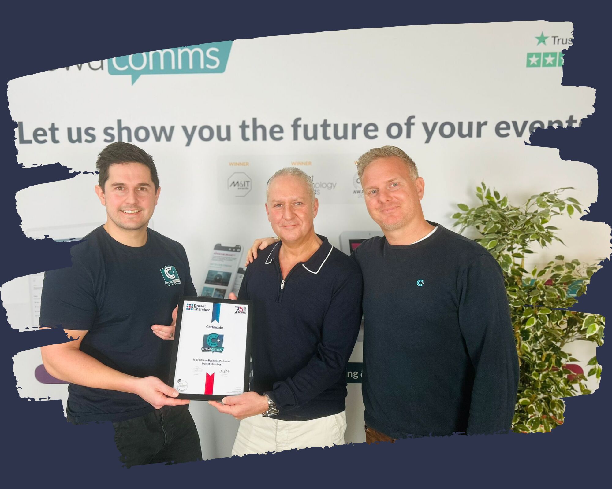 Three men holding a framed Dorset Chamber certificate naming CrowdComms a Platinum Business Partner, in front of a branded office wall