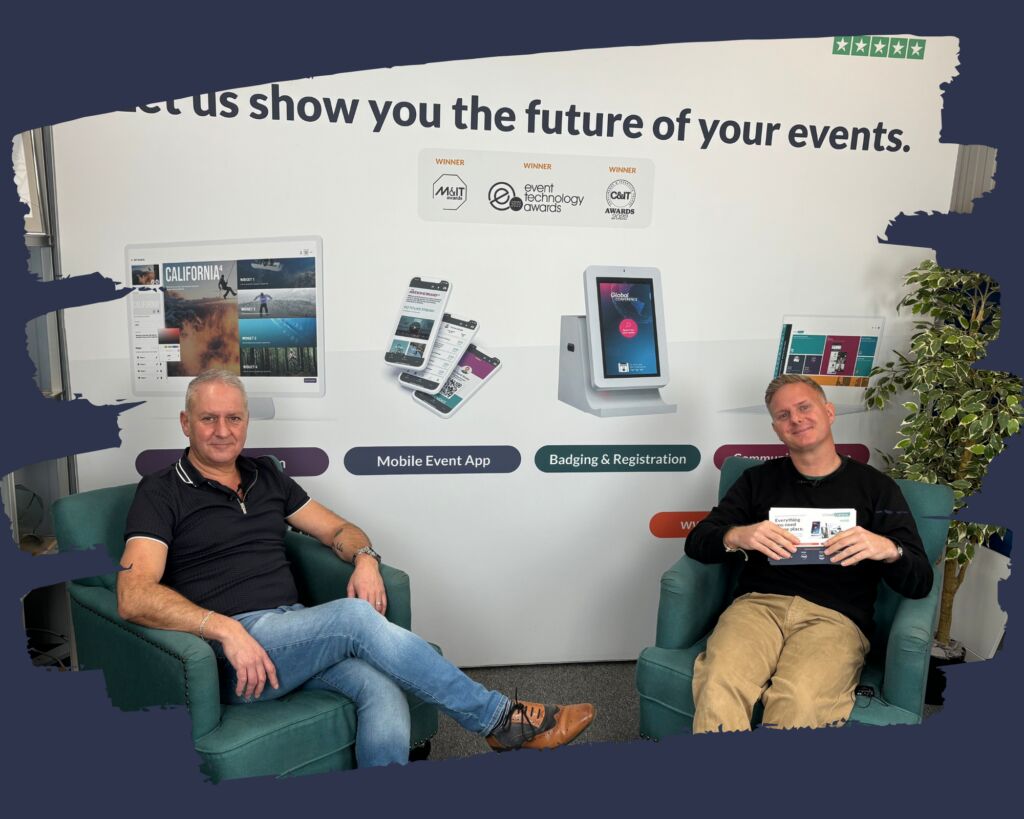 Two men seated in green armchairs in front of a CrowdComms wall graphic reading Let us show you the future of your events, with Mobile Event App and Badging and Registration labels