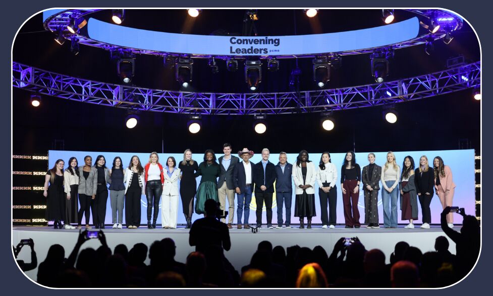 Around twenty people lined up across a wide stage under a ring of lights, the screen above reading "Convening Leaders pcma" as the audience films them
