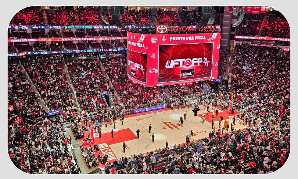 Packed basketball arena viewed from the upper tier, the centre scoreboard showing "Points for Pizza" and "Liftoff" above the Toyota Center court