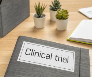 Grey ring binder labelled Clinical trial on a desk beside small potted succulents and a notepad