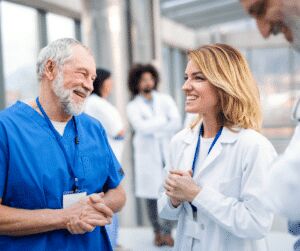 Older man in blue scrubs talking and laughing with a woman in a white coat, with two more clinicians behind them
