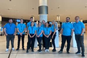 Team of nine staff in matching bright blue polo shirts and lanyards standing together in a venue foyer