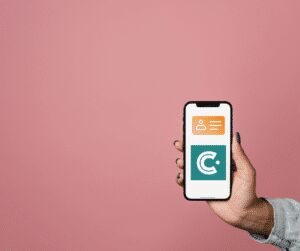 Hand holding a phone against a pink background, the screen showing a digital business card with a contact icon and the CrowdComms C logo