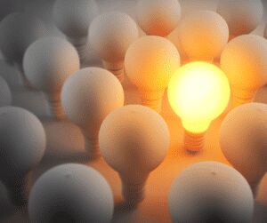 One glowing light bulb standing out among a group of unlit white bulbs