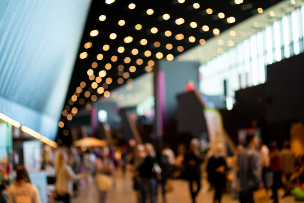 Out-of-focus exhibition hall with rows of warm ceiling downlights above a crowd of visitors