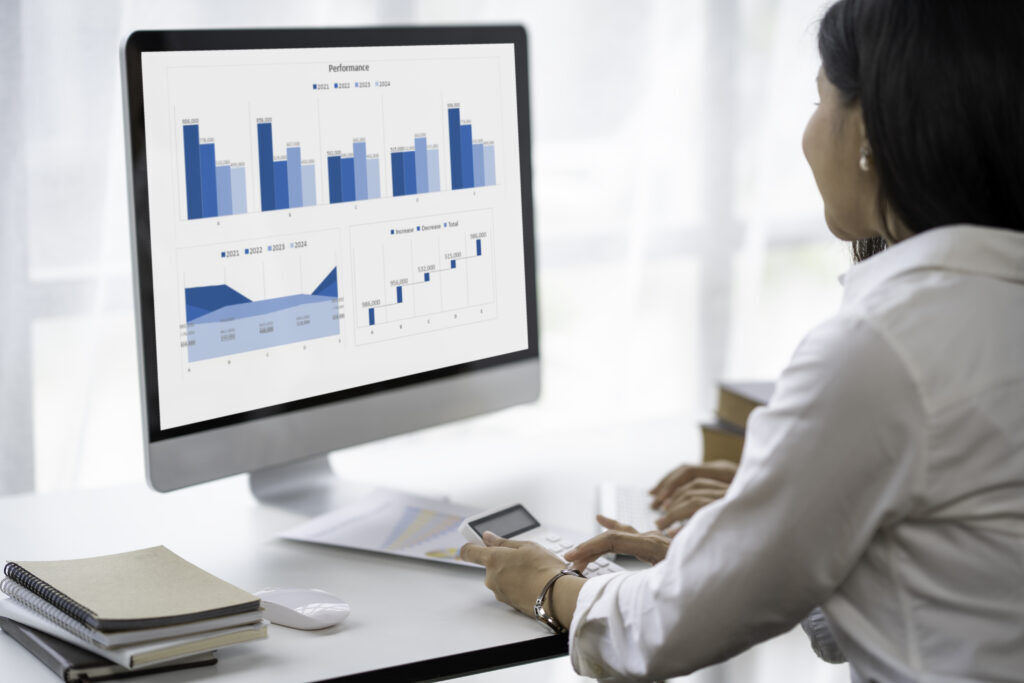 Woman at a desk reviewing a Performance dashboard of bar, area and waterfall charts on a large monitor