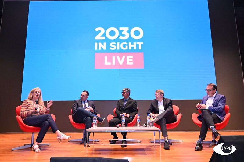 Five panellists in red armchairs on stage, one speaking into a microphone, in front of a screen reading 2030 In Sight Live