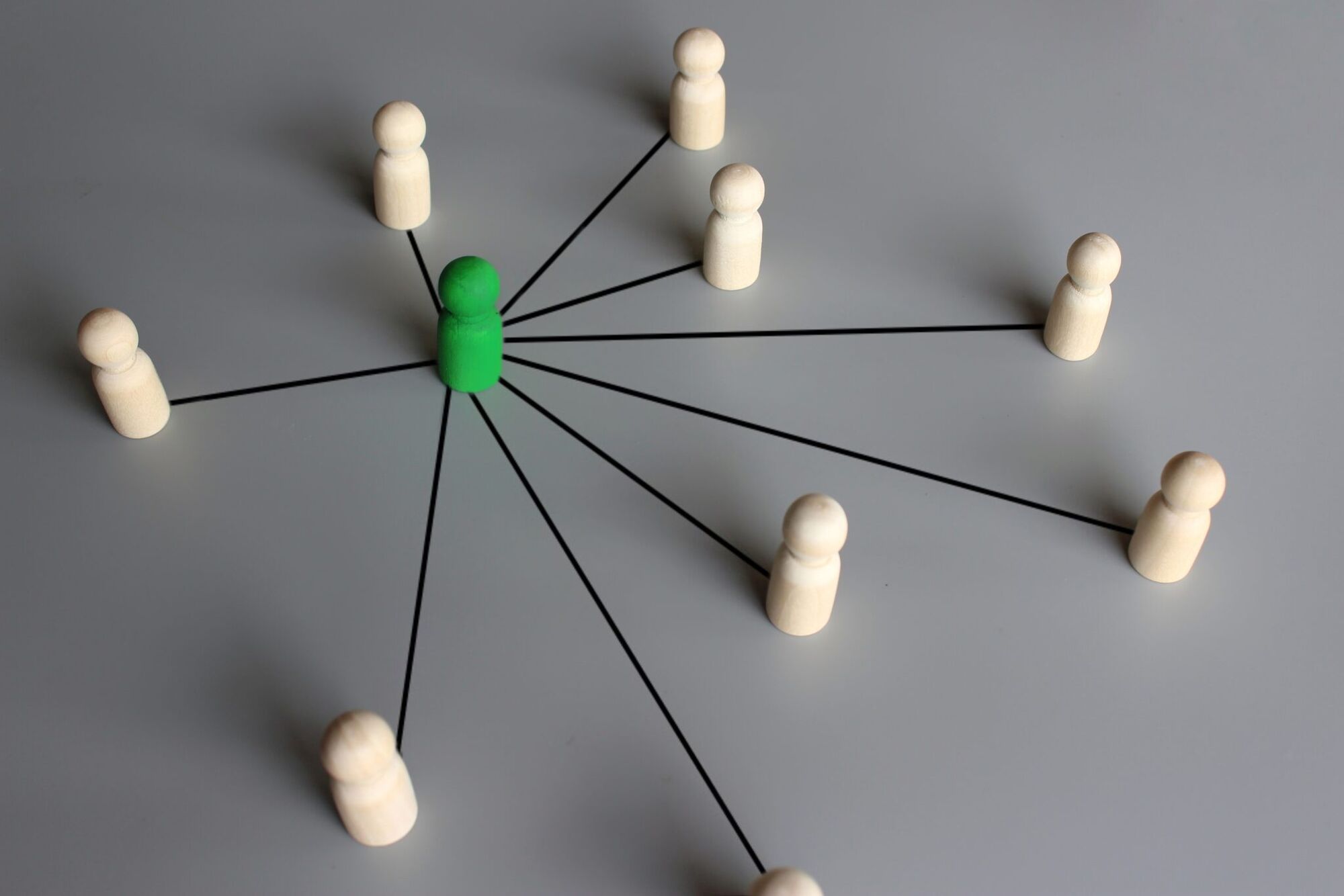 Plain wooden peg figures on a grey surface, each linked by a black line to a single green figure at the centre