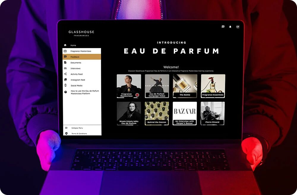 Hands typing on a laptop under red and purple lighting, the screen showing a branded Glasshouse Fragrances event page introducing Eau de Parfum with a grid of programme thumbnails