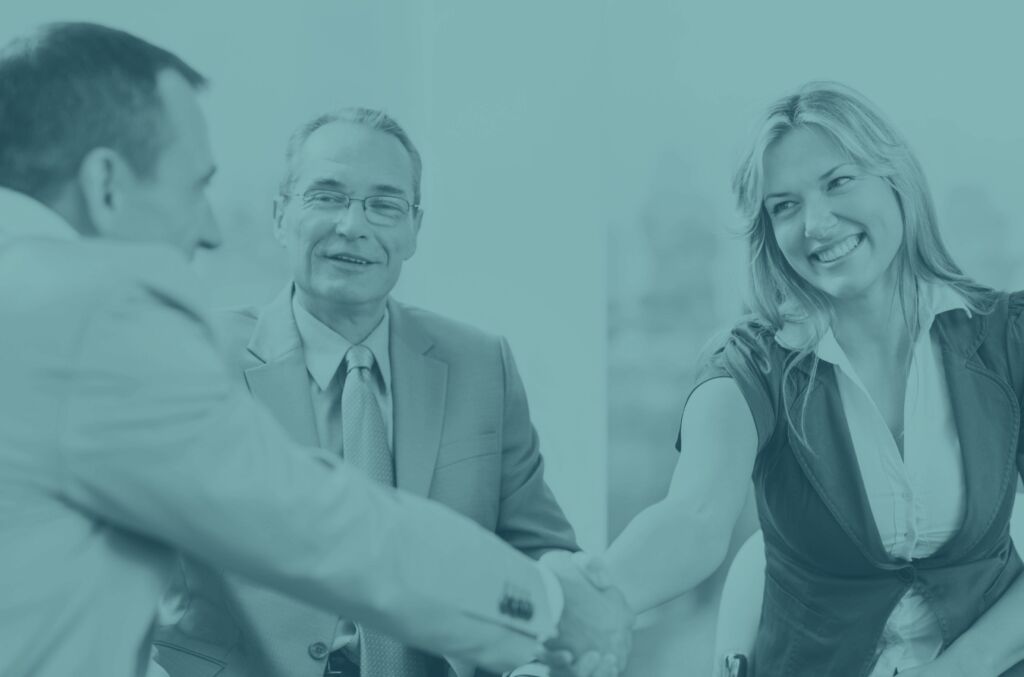 Teal-tinted photo of three business people meeting, two shaking hands while a third looks on smiling