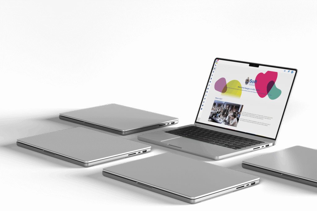 Five laptops arranged on a pale surface, the open one showing a branded event website with pink and teal graphics and a photograph